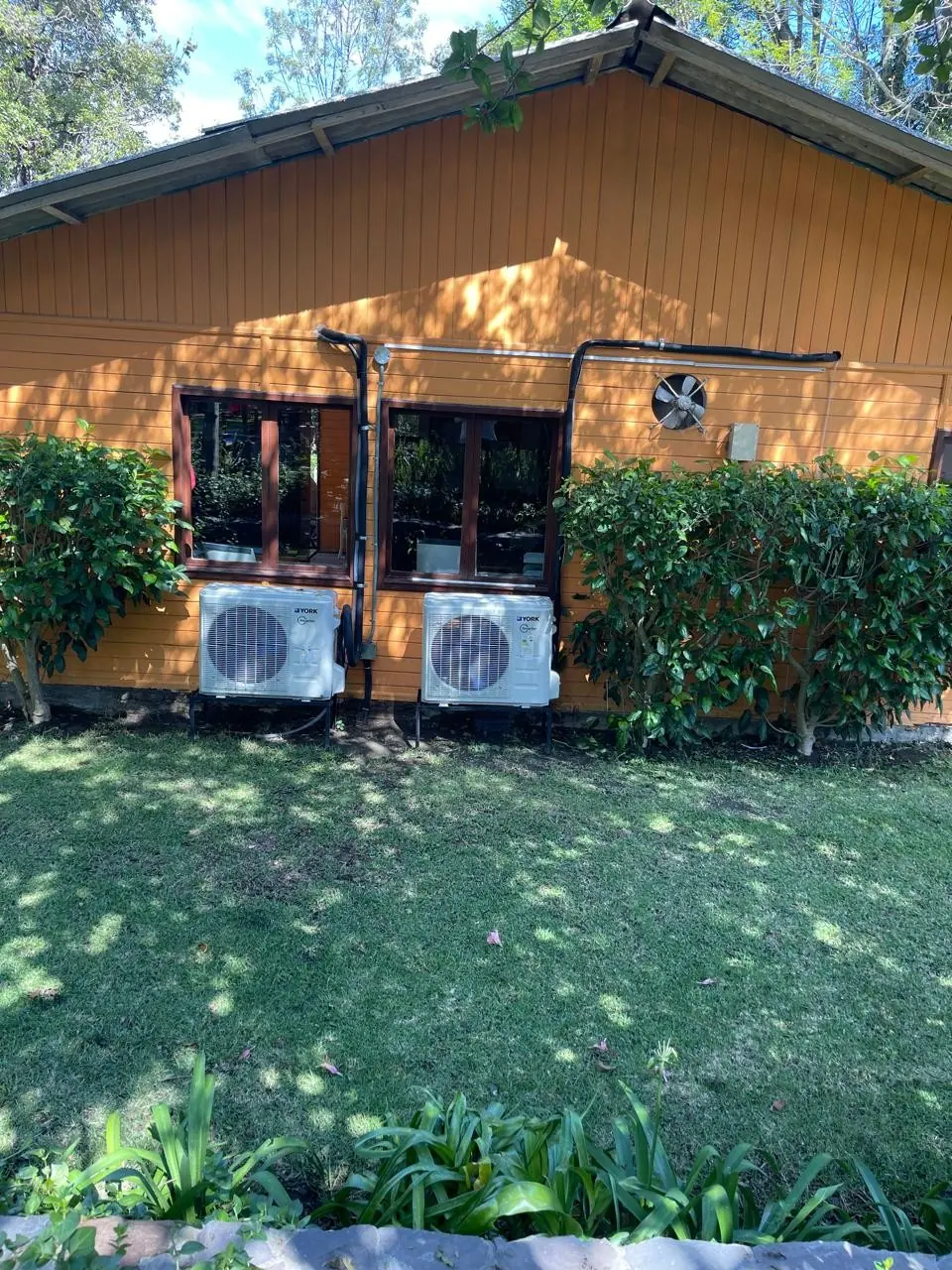 Dos unidades exteriores de aire acondicionado sobre bases, junto a una pared de madera