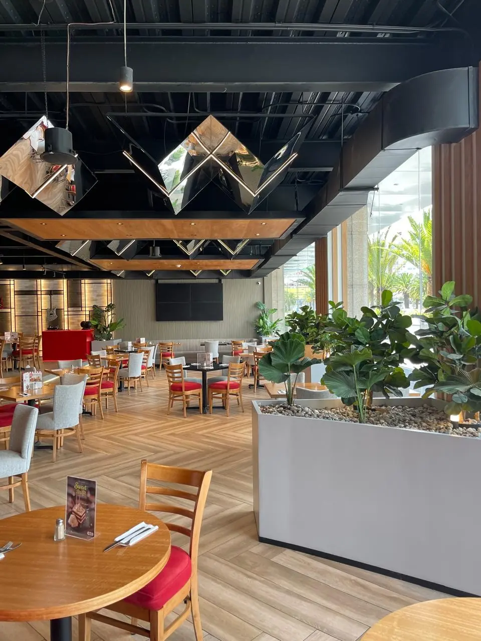 Ducto de aire negro a lo largo del ventanal de un restaurante, sobre las mesas y las jardineras